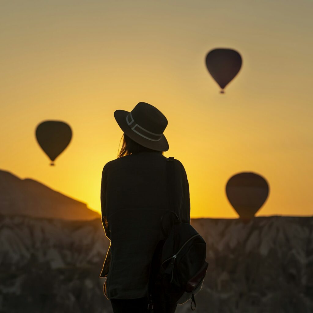 Rear view of silhouette young woman looking at hot air balloons while standing on land at Goreme, Ca