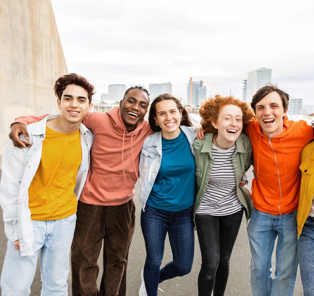 Happy group of teen friends hugging each other smiling at camera outside